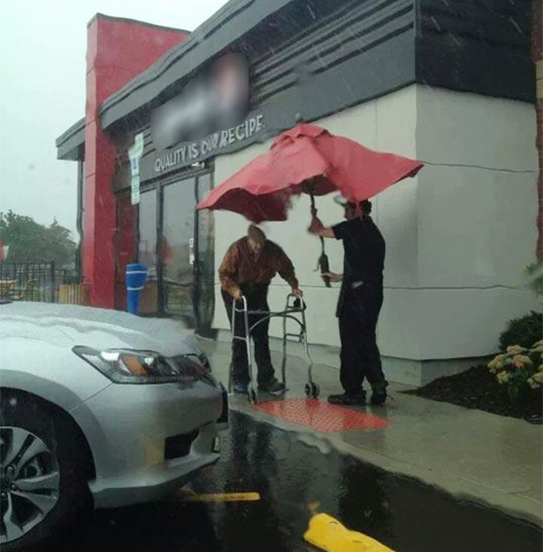 Một người bảo vệ nhổ bật cây dù che các bàn cà phê để che mưa cho một cụ già.