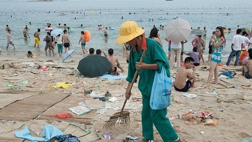 
	
	Một công nhân vệ sinh dọn dẹp rác thải xung quanh người đi tắm biển.  Ảnh: Splash News Australia.