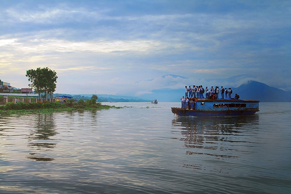 
	
	Học sinh ở Pangururan, Indonesia đứng cả lên phía trên mái của chiếc thuyền gỗ để băng qua sông. Ảnh: Muhammad Buchari.