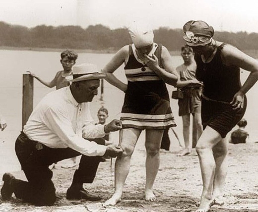 
	
	Một người đàn ông đang đo chiều dài bộ đồ bơi của những người phụ nữ để xem đồ bơi của họ có quá ngắn so với mức quy định hay không vào những năm 1920.