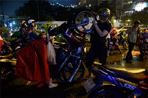 
	
	Một thanh niên đang giúp đỡ người phụ nữ dốc xe cho nước chảy ra khỏi ống pô xe máy. (Ảnh: Internet)