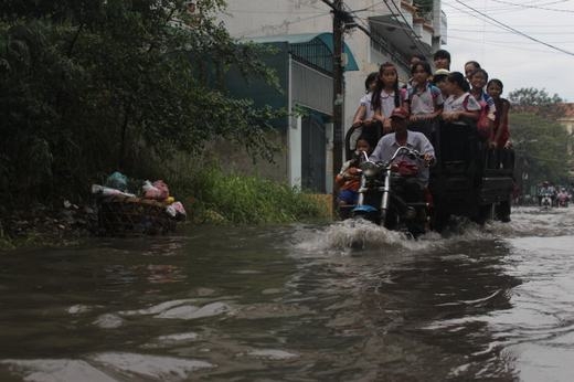 
	
	Một tài xế xe ba gác tình nguyện chở các em học sinh qua con đường ngập nước. (Ảnh: Internet)
