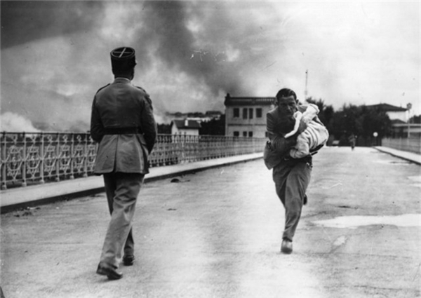 
Một nhà báo ôm một đứa trẻ chạy qua cây cầu trong cuộc nội chiến năm 1936 Tây Ban Nha.