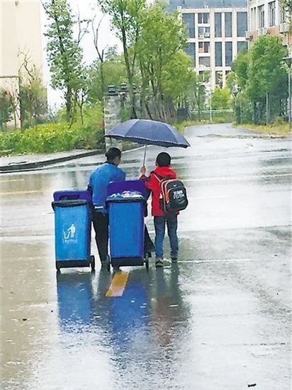 
Cậu bé tốt bụng Jian Xi đã che ô, kéo rác giúp người phụ nữ lao công giữa trời mưa to tầm tã. (Ảnh Internet)