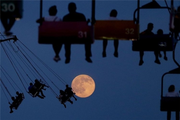 
Khoảnh khắc trùng hợp này khiến người xem cảm giác con người sắp chạm đến mặt trăng xa xôi. Ảnh chụp tại công viên trò chơi State Fair Meadowlands, East Rutherford, New Jersey.