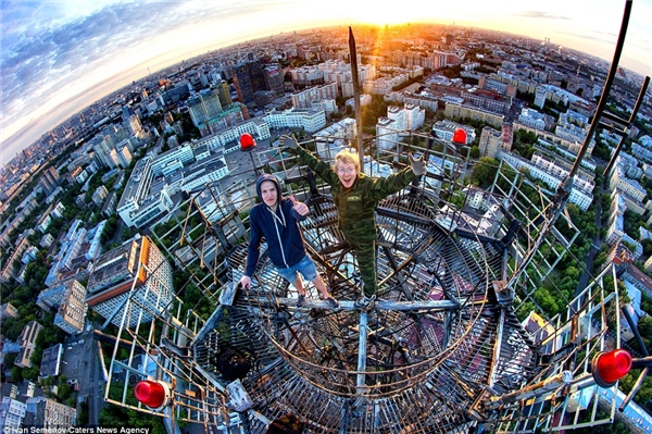 
Các chàng trai đu mình trên một tấm ván mỏng nằm phía trên một tòa tháp cao của thành phố Moscow, đằng sau là cảnh hoàng hôn tuyệt đẹp. (Ảnh: Daily Mail)