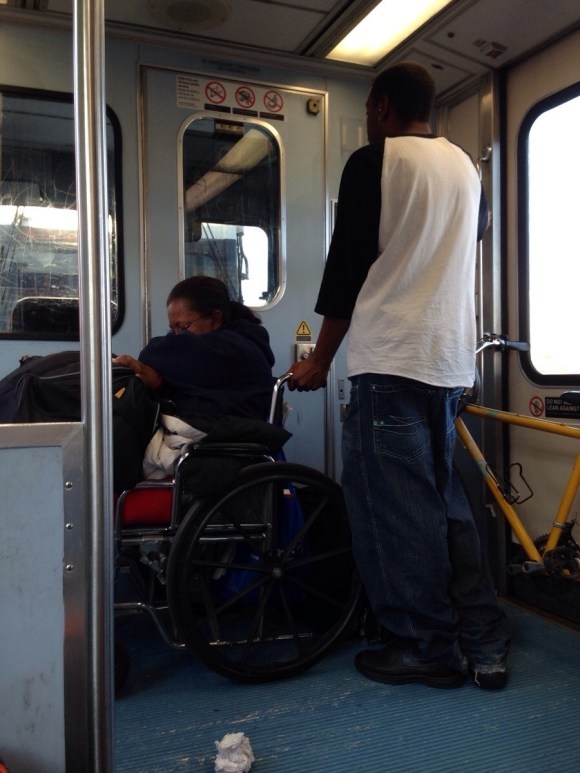 
Một hành khách đứng vịn xe lăn. (Ảnh: Internet)