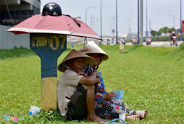 
Tại khu vực gần cầu vượt Cát Lái (quận 2), vợ chồng ông Trần Văn Nông (quận 2), cùng ngồi bên cột km, che nắng bằng chiếc dù nhỏ giữa bãi cỏ đợi khách mua những chiếc khăn đa năng.
