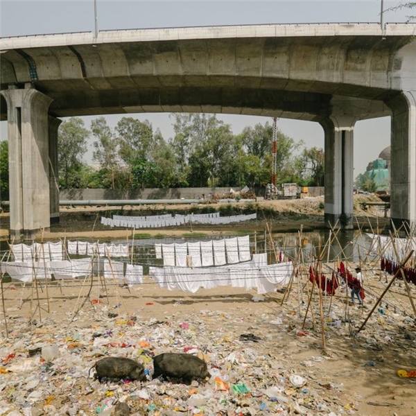 
Quần áo đã được tẩy trắng đang được hong phơi bên dưới một con cầu vượt ở Delhi, ngay bên cạnh một bãi rác và một dòng kênh vẩn đục.