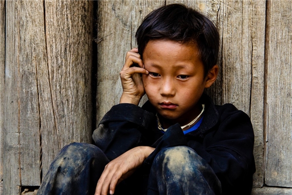 
Một bé trai người Mông ở Sủng Là, Hà Giang, bị gia đình bắt phải chụp hình với khách du lịch nhưng em không thích và ngồi buồn bên hiên nhà. Từ khi du lịch phát triển, Sủng Là nườm nượp khách ghé thăm. Một số em nhỏ bị gia đình bắt phải đi theo du khách để xin tiền hoặc đòi tiền chụp ảnh cùng. (Ảnh: Internet)