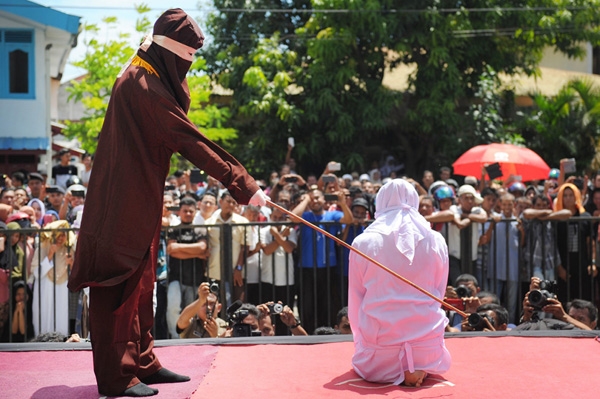 
Một người thực thi tôn giáo đang quất roi vào một thanh niên Aceh như sự trừng phạt cho việc hẹn hò ngoài hôn nhân, trái với pháp luật Sharia bên ngoài thánh đường ở Banda Aceh, Indonesia. Người Aceh ngày càng trở nên bảo thủ hơn trong những năm gần đây và là dân tộc duy nhất ở Indonesia còn áp dụng luật Sharia.
