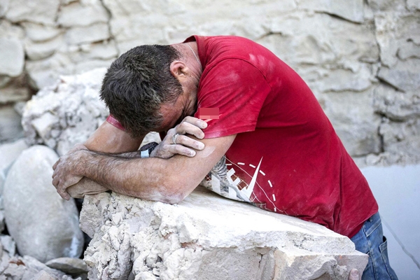 
Một người đàn ông đang tựa vào đống đổ nát để giấu đi nỗi đau của mình sau trận động đất ở Amatrice. 